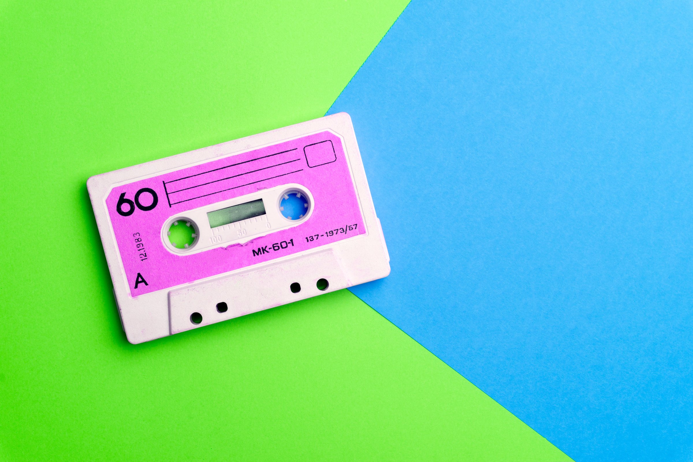 Retro old school 80-s or 90-s concept. Audio cassette on a bright blue-pink background